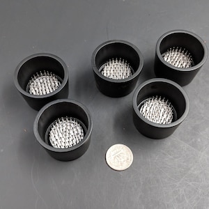 May include: Five black plastic floral frog bases with silver metal pins. The bases are round and have a diameter of approximately 3 inches.