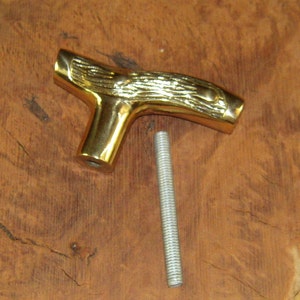 May include: A gold-colored metal T-shaped handle with a woodgrain design. The handle is attached to a silver-colored metal rod.