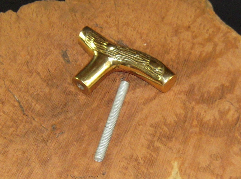 May include: A gold-colored metal cane handle with a detailed wood grain design. The handle is shaped like a tree branch and has a threaded hole for attaching a cane shaft.
