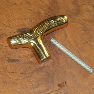 May include: A gold-colored metal T-shaped handle with a woodgrain design. The handle has a threaded hole in the bottom and comes with a separate threaded metal rod.