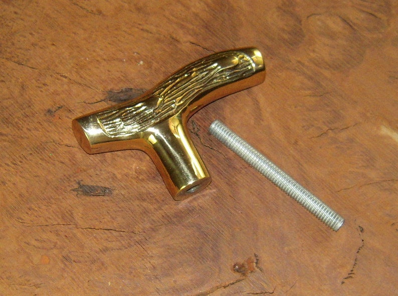 May include: A gold-colored metal T-shaped handle with a woodgrain design. The handle has a threaded hole in the bottom and comes with a separate threaded metal rod.