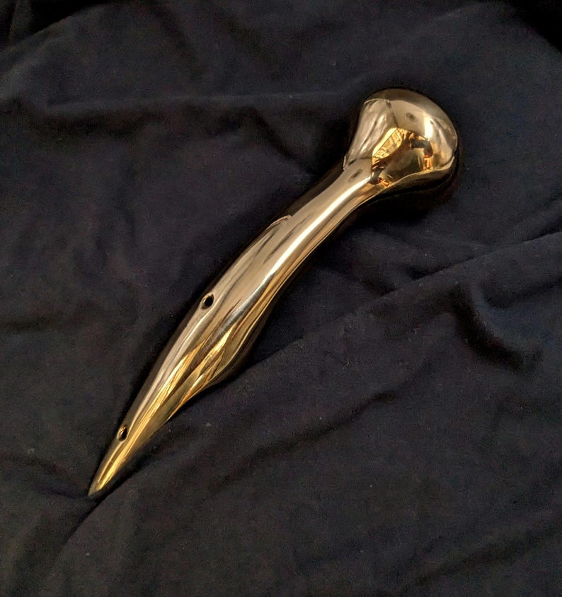 Puede incluir: Una manija de metal pulido de color dorado con un extremo redondeado y una punta puntiaguda. La manija tiene tres peque&ntilde;os agujeros perforados.