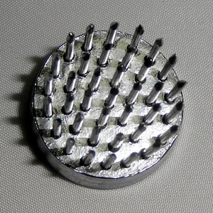 Peut inclure: Un outil circulaire en m&eacute;tal argent&eacute; avec une base et de nombreux petits piquets m&eacute;talliques pointus qui d&eacute;passent du dessus.