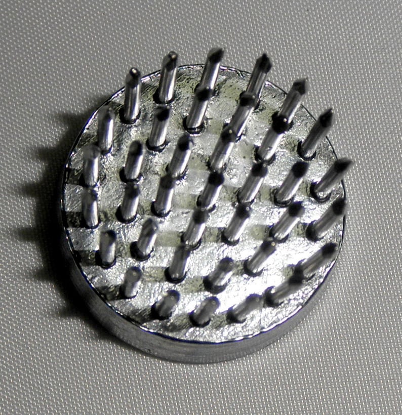 Peut inclure: Un outil circulaire en m&eacute;tal argent&eacute; avec une base et de nombreux petits piquets m&eacute;talliques pointus qui d&eacute;passent du dessus.