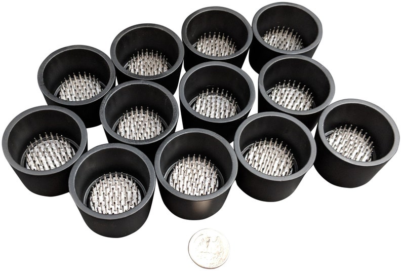 May include: Twelve black floral foam holders with silver pins. The holders are arranged in a circle with a silver coin in the center.