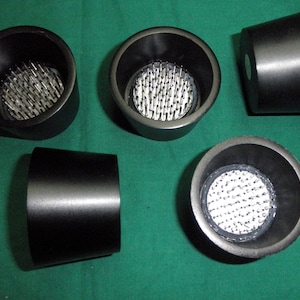 May include: Five black floral foam blocks with a pincushion design. The foam blocks are round and have a flat bottom. The pincushions are made of metal pins that are arranged in a grid pattern.