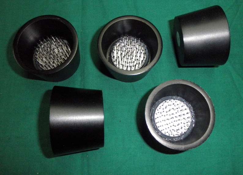 May include: Five black floral foam blocks with a pincushion design. The foam blocks are round and have a flat bottom. The pincushions are made of metal pins that are arranged in a grid pattern.