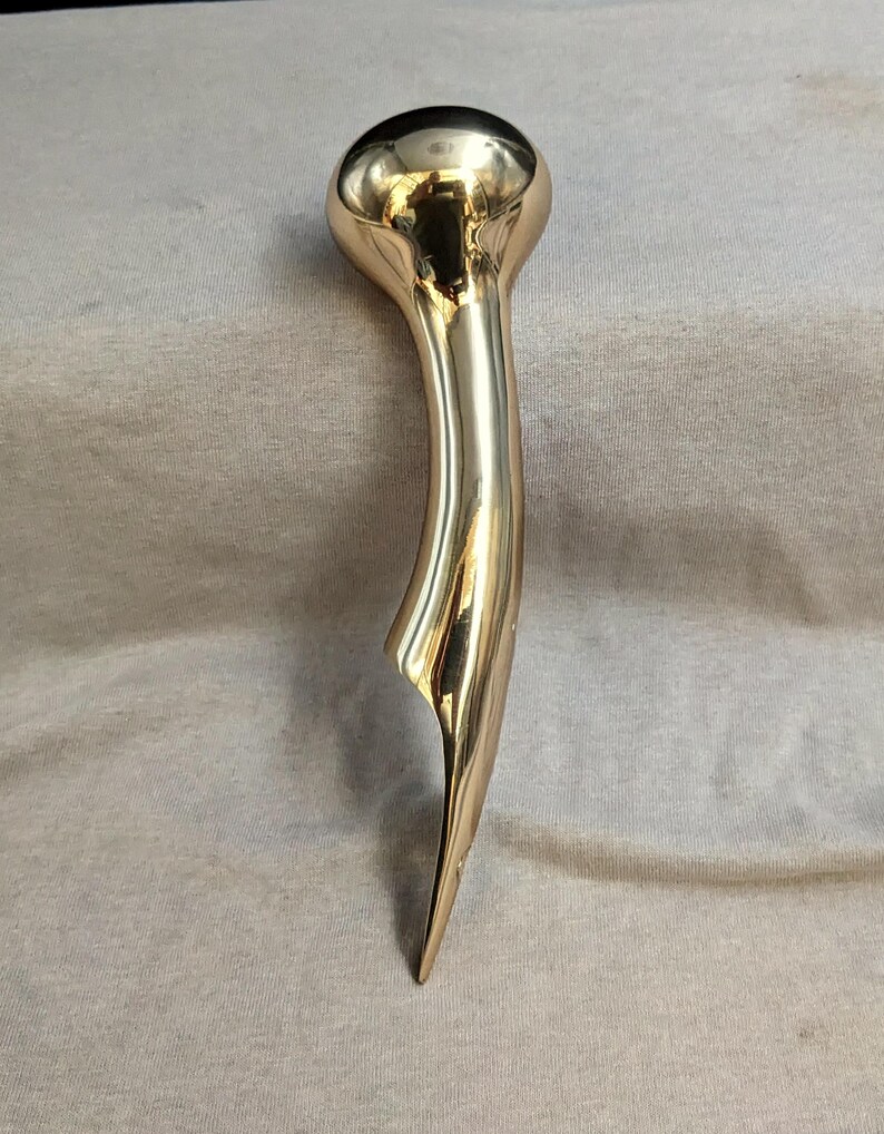 Puede incluir: Una escultura de metal pulido de color dorado con una parte superior redondeada y una parte inferior larga, curva y puntiaguda.