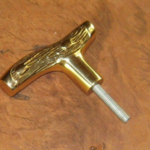 May include: A gold-toned metal T-shaped cabinet knob with a detailed antler design. The knob has a threaded screw for installation.