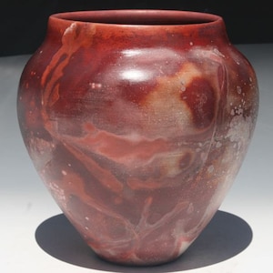 May include: A red ceramic vase with a marbled glaze pattern. The vase has a rounded body and a wide opening.