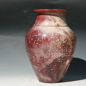 May include: A handcrafted, decorative vase with a bulbous body and a flared rim. The vase features a rich, mottled burgundy and cream color palette with speckled detailing. The ceramic vessel is a unique piece of home decor.