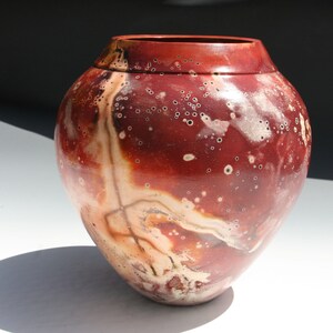 May include: A red and white ceramic vase with a speckled glaze. The vase has a round body and a wide opening.