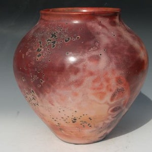 May include: A red ceramic vase with a speckled glaze. The vase has a round body and a wide opening.