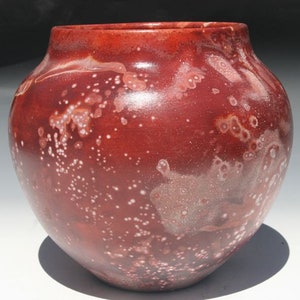 May include: A red ceramic vase with a speckled white glaze. The vase has a rounded body and a wide opening.