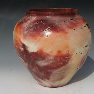 May include: A ceramic vase with a rounded body and a wide mouth. The vase is decorated with a mottled glaze in shades of red, orange, and white.
