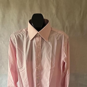 Puede incluir: Una camisa rosa claro con cuello y pu&ntilde;os rosa claro en contraste. La camisa de manga larga tiene una parte delantera abotonada y se muestra en un maniqu&iacute; negro.