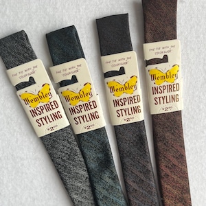 May include: Four narrow neckties in shades of grey, teal, brown, and burgundy, each with a textured pattern. Each tie is packaged with a white label featuring the text "Wembley INSPIRED STYLING" and a butterfly graphic. The labels also include the text "THE TIE WITH THE COLOR GUIDE".