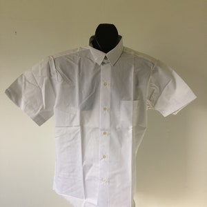 Puede incluir: Una camisa blanca de manga corta con botones y un bolsillo en el lado izquierdo.