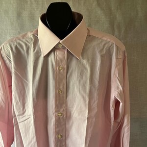 Puede incluir: Una camisa rosa claro con cuello cl&aacute;sico y mangas largas. La camisa est&aacute; abotonada en la parte delantera con botones peque&ntilde;os y redondos. La camisa se exhibe en una cabeza de maniqu&iacute; negra.
