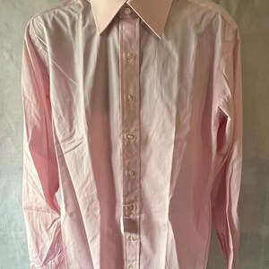 Puede incluir: Una camisa rosa claro con cuello cl&aacute;sico y cierre de botones. La camisa de manga larga se exhibe en un maniqu&iacute; negro. La camisa tiene un corte entallado y est&aacute; hecha de una tela suave.