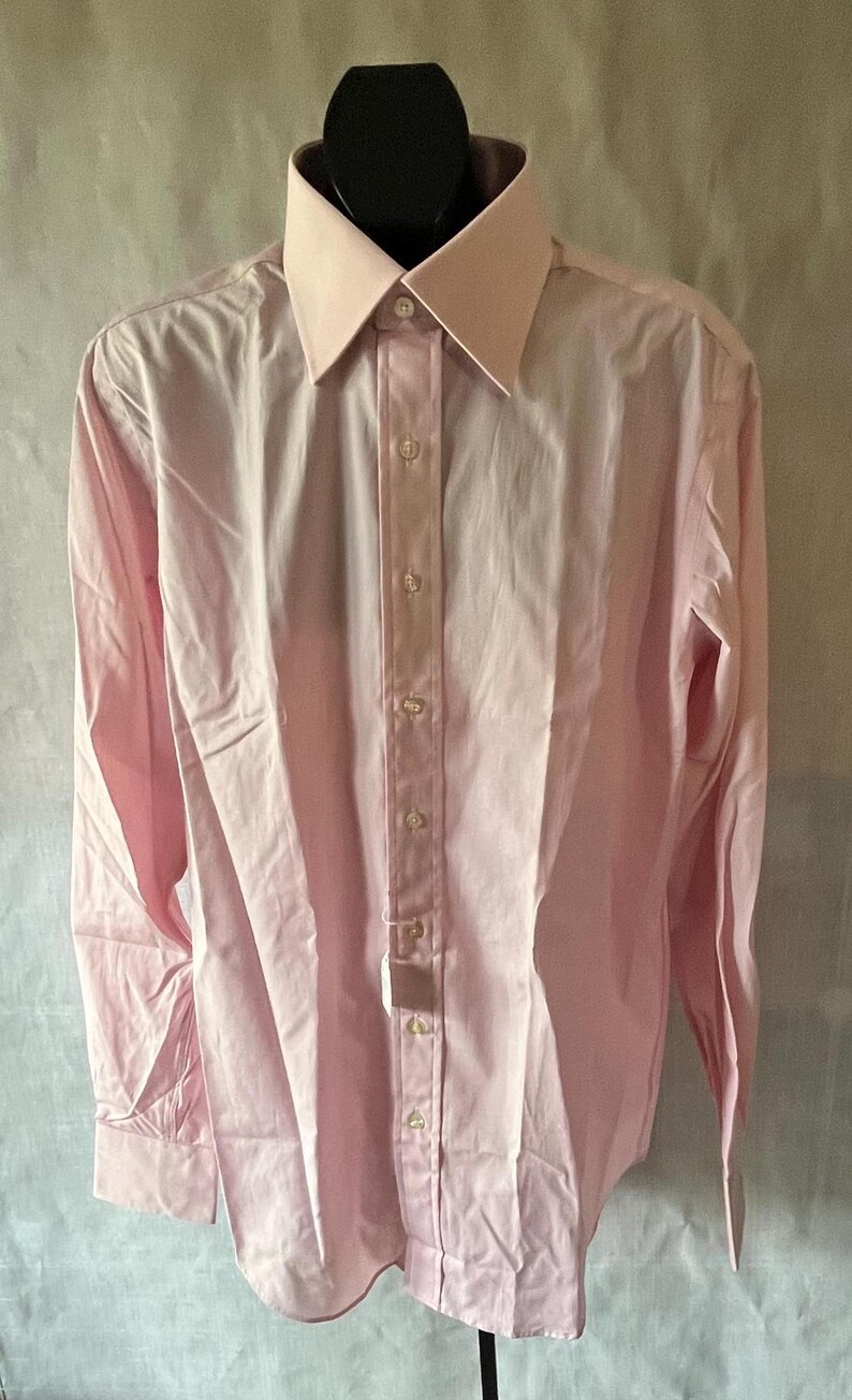 Puede incluir: Una camisa rosa claro con cuello cl&aacute;sico y cierre de botones. La camisa de manga larga se exhibe en un maniqu&iacute; negro. La camisa tiene un corte entallado y est&aacute; hecha de una tela suave.