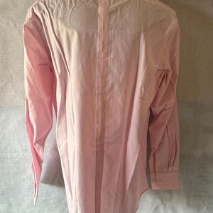 Puede incluir: Camisa rosa claro de manga larga, vista desde la espalda, exhibida en un maniqu&iacute;. La camisa tiene un cuello cl&aacute;sico, pu&ntilde;os abotonados y una costura vertical en el centro de la espalda. La tela parece ser de algod&oacute;n ligero o una mezcla similar.