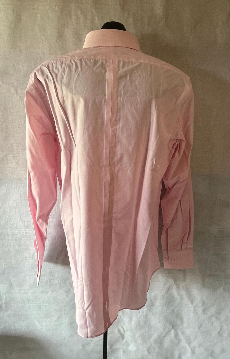 Puede incluir: Camisa rosa claro de manga larga, vista desde la espalda, exhibida en un maniqu&iacute;. La camisa tiene un cuello cl&aacute;sico, pu&ntilde;os abotonados y una costura vertical en el centro de la espalda. La tela parece ser de algod&oacute;n ligero o una mezcla similar.