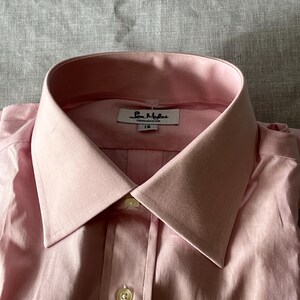 Puede incluir: Camisa rosa claro con cuello cl&aacute;sico y abotonadura. La camisa tiene una etiqueta que dice "Sam Myles DESIGNATURE" y la talla "16". La camisa est&aacute; hecha de una tela suave.