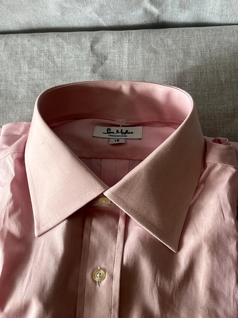 Puede incluir: Camisa rosa claro con cuello cl&aacute;sico y abotonadura. La camisa tiene una etiqueta que dice "Sam Myles DESIGNATURE" y la talla "16". La camisa est&aacute; hecha de una tela suave.