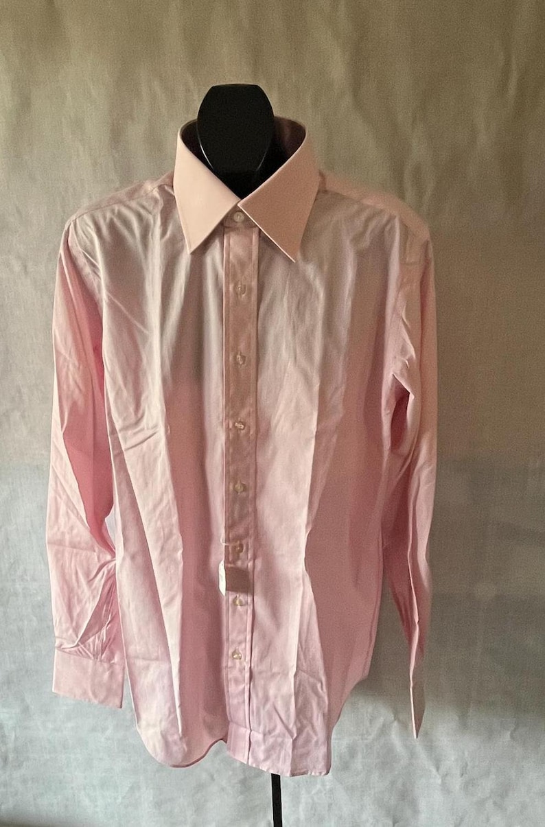 Puede incluir: Una camisa rosa claro con cuello y pu&ntilde;os rosa claro en contraste. La camisa de manga larga tiene una parte delantera abotonada y se muestra en un maniqu&iacute; negro.
