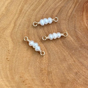 May include: Three gold-toned wire connectors with three white pearl beads on each connector. The connectors are on a wooden surface.