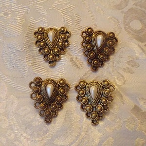 May include: Four gold-tone metal embellishments with a teardrop-shaped pearl in the center. Each embellishment has a decorative design of small circles and beads.