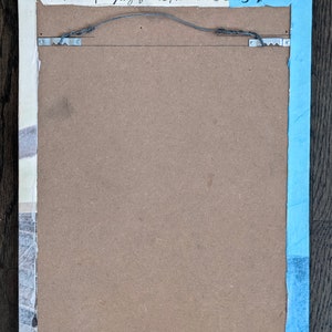 Puede incluir: La parte posterior de una obra de arte enmarcada con un borde azul claro. El marco es de madera y tiene un respaldo de cart&oacute;n marr&oacute;n. La firma del artista, "Mary Julia Tunnell 2015", est&aacute; escrita con tinta negra en la esquina superior derecha.