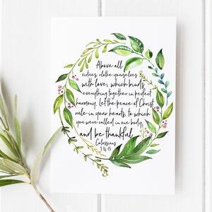 Puede incluir: Una ilustración de acuarela de una corona de hojas con flores rosas. La corona rodea una cita de Colosenses 3:14-15: "Sobre todo, revestíos de amor, que es el vínculo de la perfección. Y que la paz de Cristo reine en vuestros corazones, a la que también fuisteis llamados en un solo cuerpo."