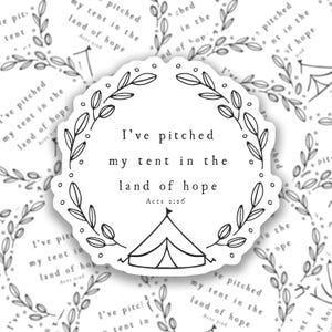 May include: A black and white sticker with a floral wreath design. The sticker features the text "I've pitched my tent in the land of hope" with the Bible verse "Acts 2:26" underneath. A small tent icon is at the bottom of the sticker.