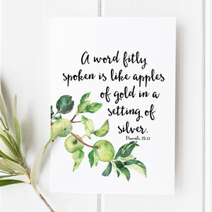 May include: A white print featuring the quote "A word fitly spoken is like apples of gold in a setting of silver." The print includes a watercolor illustration of green apples and leaves. The text "Proverbs 25:11" is at the bottom.