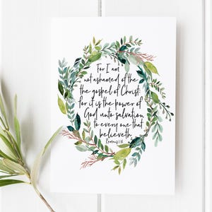 Könnte beinhalten: Ein weißer rechteckiger Druck mit einem Aquarellkranz aus grünen und salbeifarbenen Blättern, der den schwarzen Text umgibt: For I am not ashamed of the gospel of Christ: for it is the power of God unto salvation to every one that believeth. Romans 1:16.