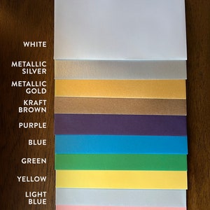 May include: A collection of 14 different colored cardstock paper samples, including white, metallic silver, metallic gold, kraft brown, purple, blue, green, yellow, light blue, pink, and red.