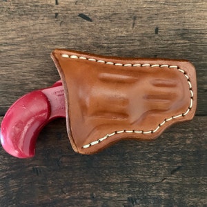 May include: A red plastic toy gun in a brown leather holster with white stitching.