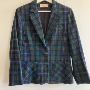 May include: A long-sleeve blazer featuring a dark blue and green plaid pattern with thin yellow lines. The garment includes a notched lapel, three front buttons, two lower patch pockets, one chest pocket, and three small buttons on each sleeve cuff.