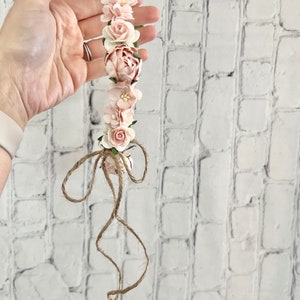 May include: A pink flower crown with a brown twine bow. The crown is made of paper flowers and is perfect for a special occasion.