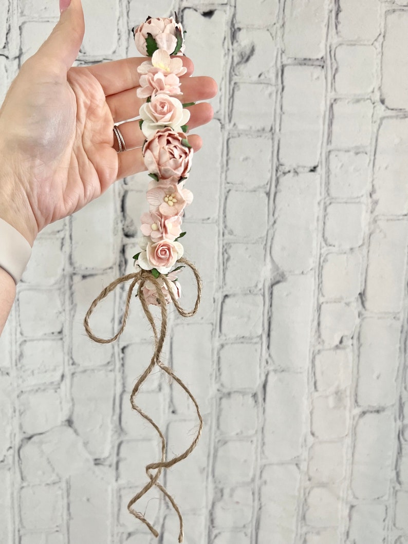 May include: A pink flower crown with a brown twine bow. The crown is made of paper flowers and is perfect for a special occasion.