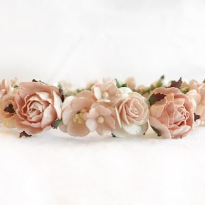 May include: A delicate flower crown made of blush pink and white paper flowers. The crown is perfect for a wedding, bridal shower, or other special occasion.
