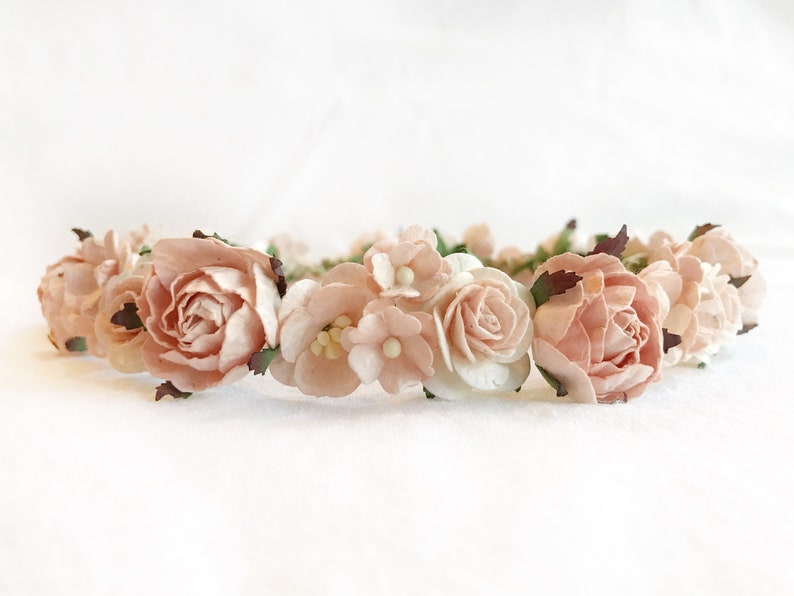 May include: A delicate flower crown made of blush pink and white paper flowers. The crown is perfect for a wedding, bridal shower, or other special occasion.