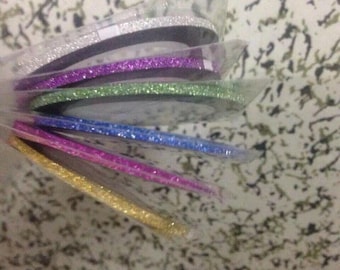 Puede incluir: Un conjunto de cintas de purpurina de colores variados, incluyendo plata, morado, verde, azul, rosa y dorado. Cada cinta está cuidadosamente empaquetada, mostrando los colores vibrantes y el acabado brillante. Ideal para manualidades y proyectos decorativos.