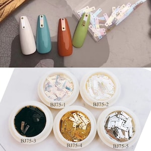 Puede incluir: Cinco recipientes de pequeñas lentejuelas rectangulares iridiscentes con acentos dorados. Los recipientes están etiquetados como BJ75-1, BJ75-2, BJ75-3, BJ75-4 y BJ75-5. Las lentejuelas son de varios colores, incluyendo blanco, negro, dorado e iridiscente.