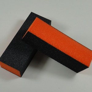 Peut inclure: Deux limes à ongles noires et orange. Les limes sont rectangulaires et ont une surface rugueuse. Le côté orange est sur le côté noir.
