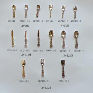 May include: A set of miniature silver and gold cutlery, including spoons, forks, and knives. The cutlery is arranged in rows on a white background. The measurements of each piece are listed below each item.