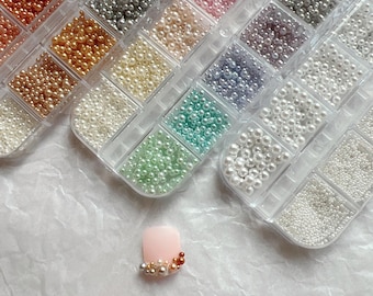 Pode incluir: Variedade de pequenas contas coloridas em recipientes de plástico transparente. As contas são de várias cores, incluindo dourado, prateado, rosa e verde. Uma única unha rosa com contas decorativas também é visível.