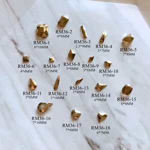 Peut inclure: Assortiment de strass en métal doré de différentes formes et tailles. Chaque strass est étiqueté avec un code et des mesures en millimètres.